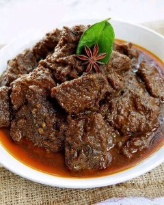 Rendang daging sapi khas Minangkabau dengan bumbu pekat berwarna cokelat tua, disajikan hangat di atas piring 