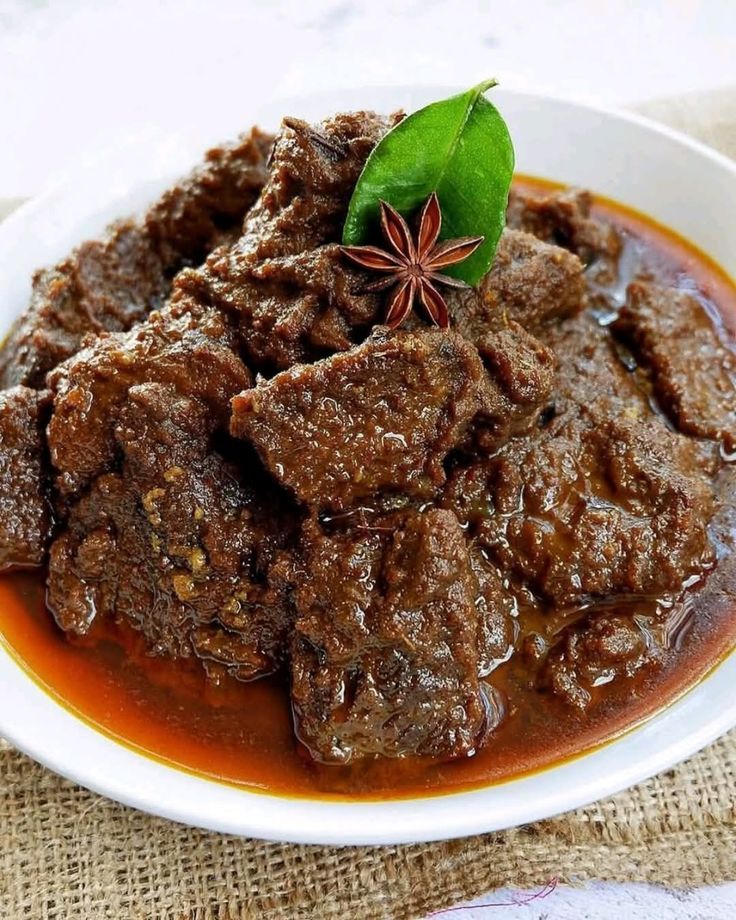 Rendang daging sapi khas Minangkabau dengan bumbu pekat berwarna cokelat tua, disajikan hangat di atas piring